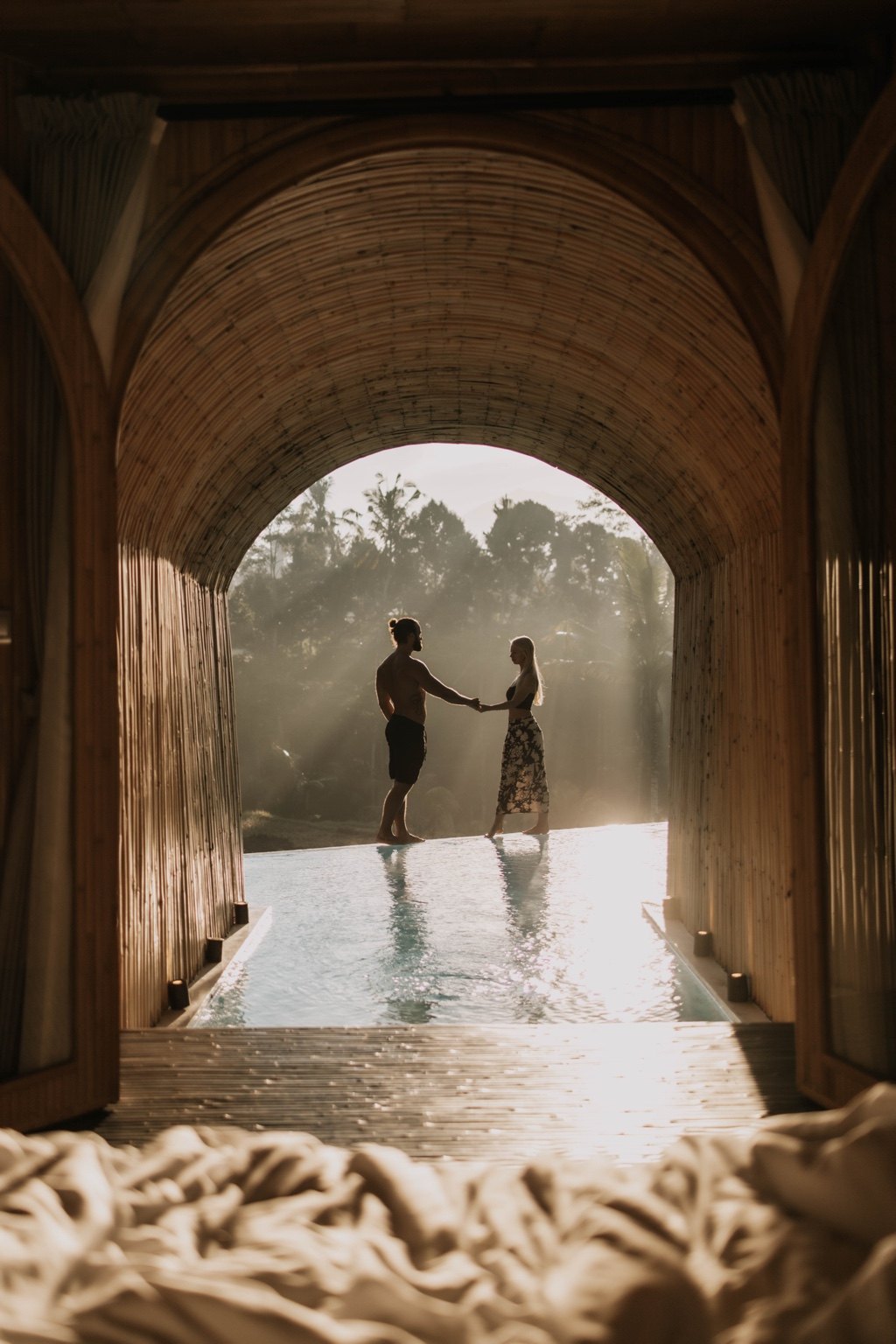 A couple holding hands by a pool in warm tropical light